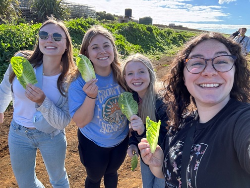 Caroline stands with friends while holding up leaves of lettuce