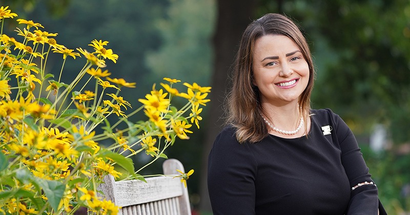 Haley Oliver sitting on a wooden bench surrounded by yellow flowers