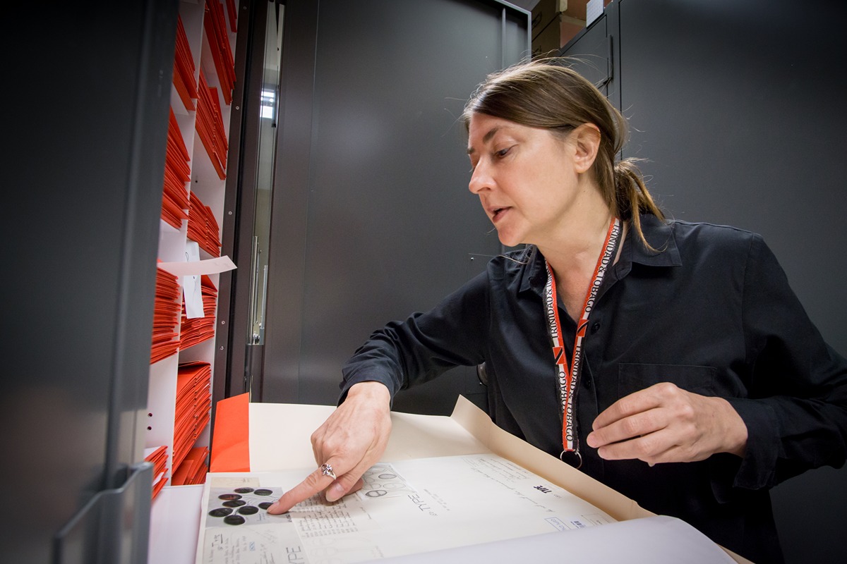 Catherine Aime points at a picture of fungi in a red folder form the Purdue Herbaria lockers