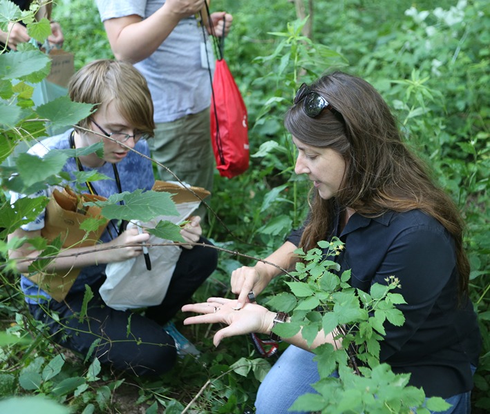 Catherine Aime sitting in the woods with students, showing them small fungi in the palm off her hand