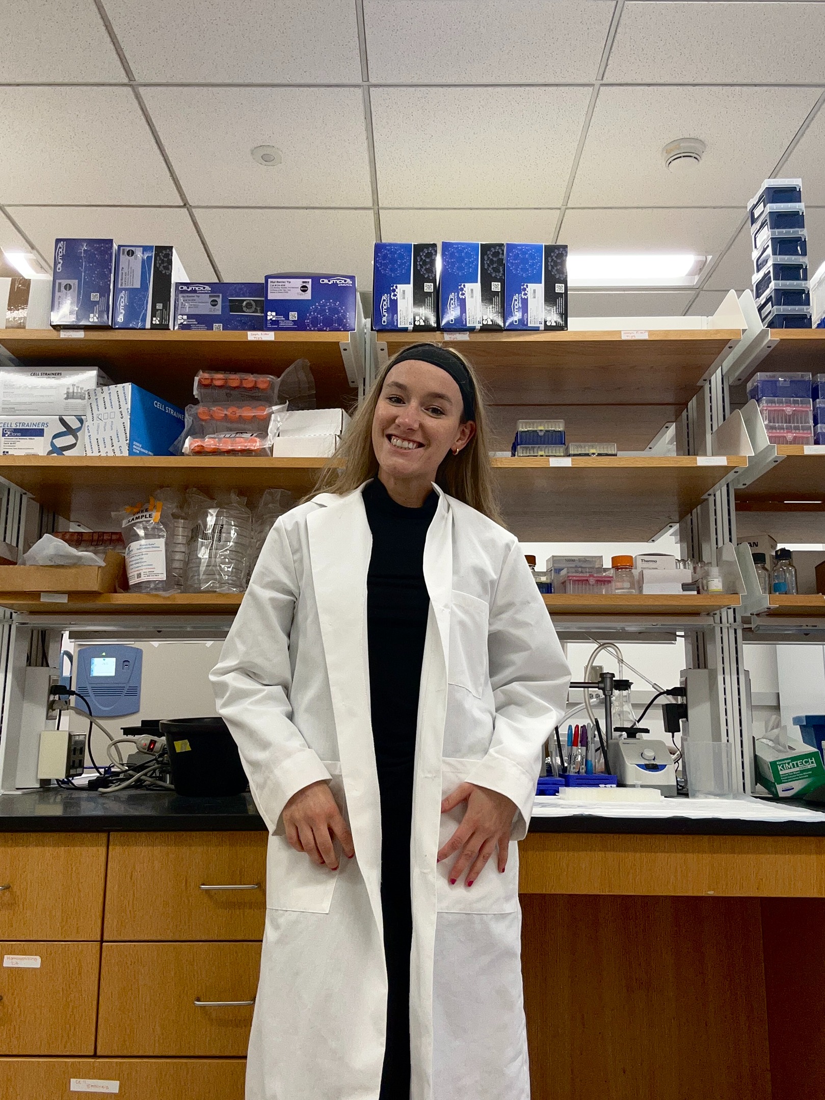 Bryn Yoder stands in a lab coat in front on a counter with beakers