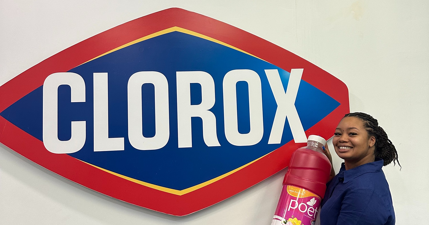 Kayla Hinton stands in front of a Clorox logo on a wall with a giant prop of a cleaning bottle