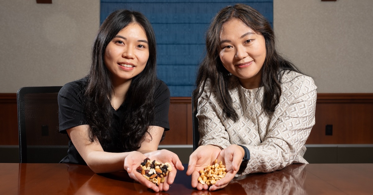 Two researchers seated at a conference table smile at the camera while holding nuts and trail mix.