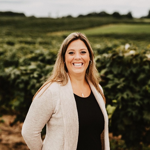 Nancie Oxley stands in grape field at vineyard.