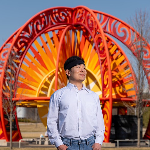 Yaguang Zhang stands in front of the orange sun sculpture at Purdue