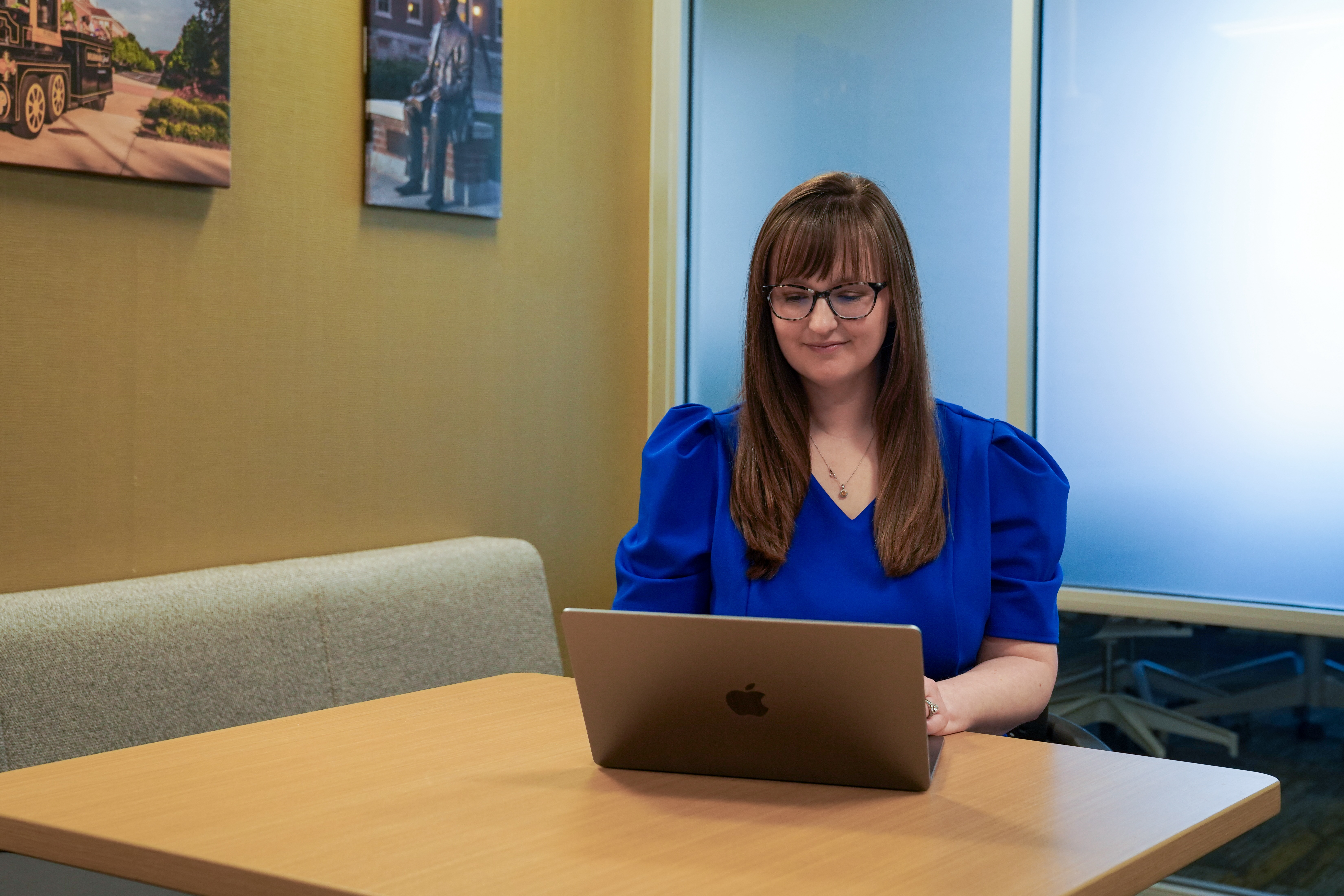 Brenna Ellison working on her laptop with two photographs of Purdue landmarks, the Boilermaker Special and the John Purdue statue, in the background