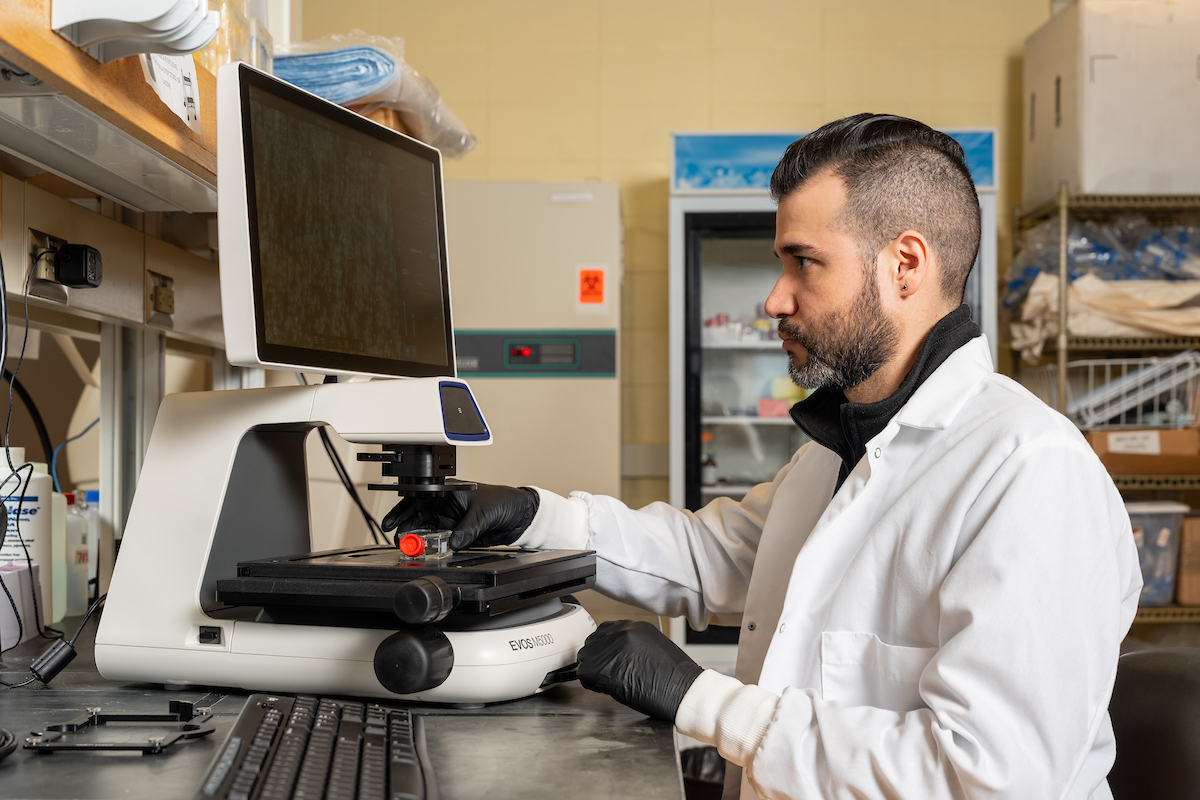 Pietri in white lab quote sitting in front of a microscope