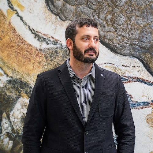 Luiz Brito smiling with a mural of cows in the background.