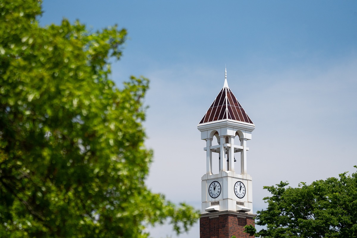 The Purdue Bell Tower behind some green tree branches