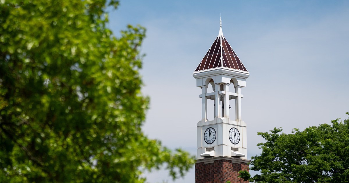 The Purdue Bell Tower behind some green tree branches