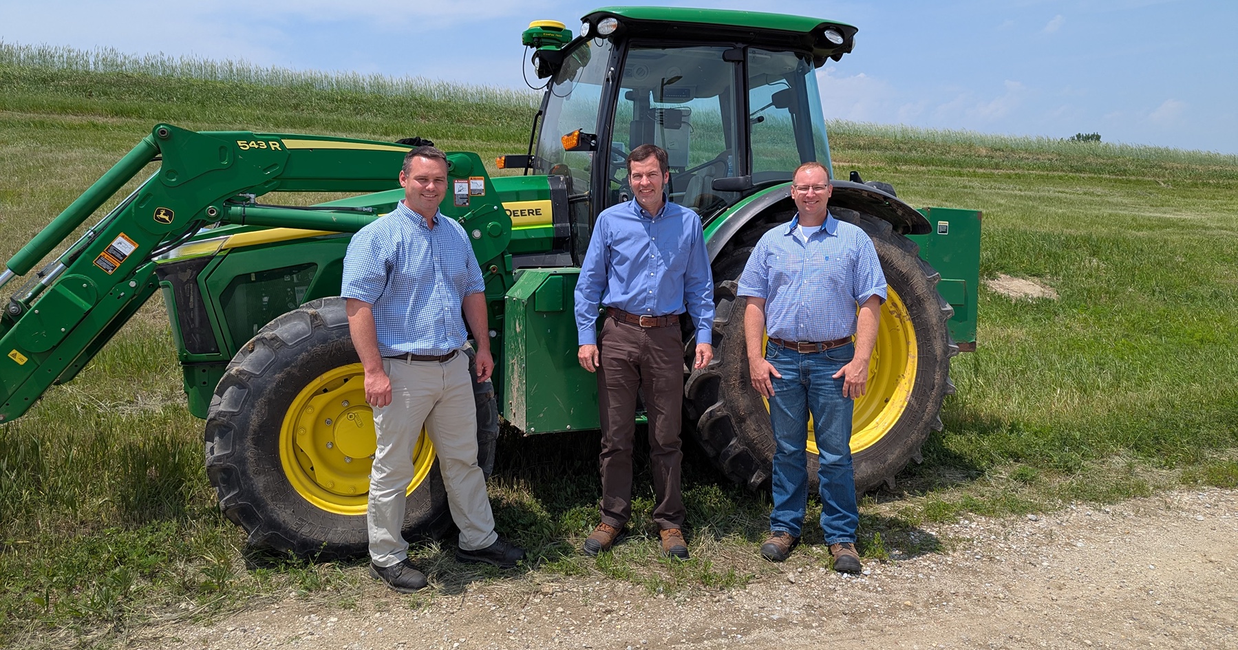 Purdue Alumni and John Deere employees stand by a tractor they have had a part in designing.