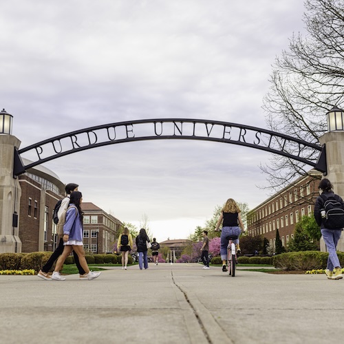 Students walking and bicycling under the Purdue University arch this summer.