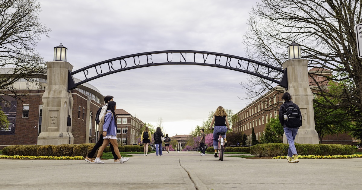Students walking and bicycling under the Purdue University arch this summer.