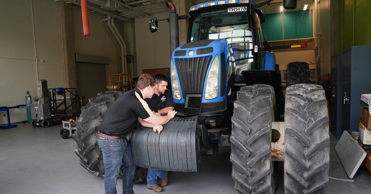 Graduate students standing in front of a tractor while working on a laptop.