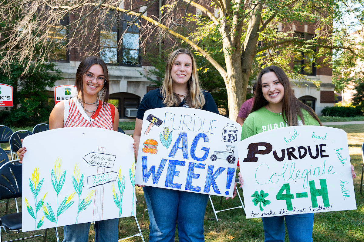 Three students holding signs, cheering on panelists at the AgDay College Roadshow