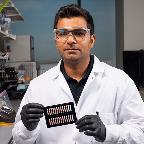  Purdue research scientist Bilal Ahmed examines a microfluidic paper-based biosensor cartridge under light to display the visible results of an assay for genetically modified crop traits.