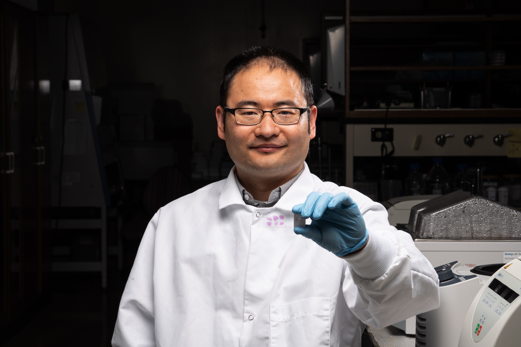 Weicang Wang, wearing a white lab coat, holds a slide with tissue cross sections