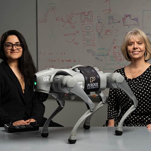Kaur and Hill stand by robotic dog on a table