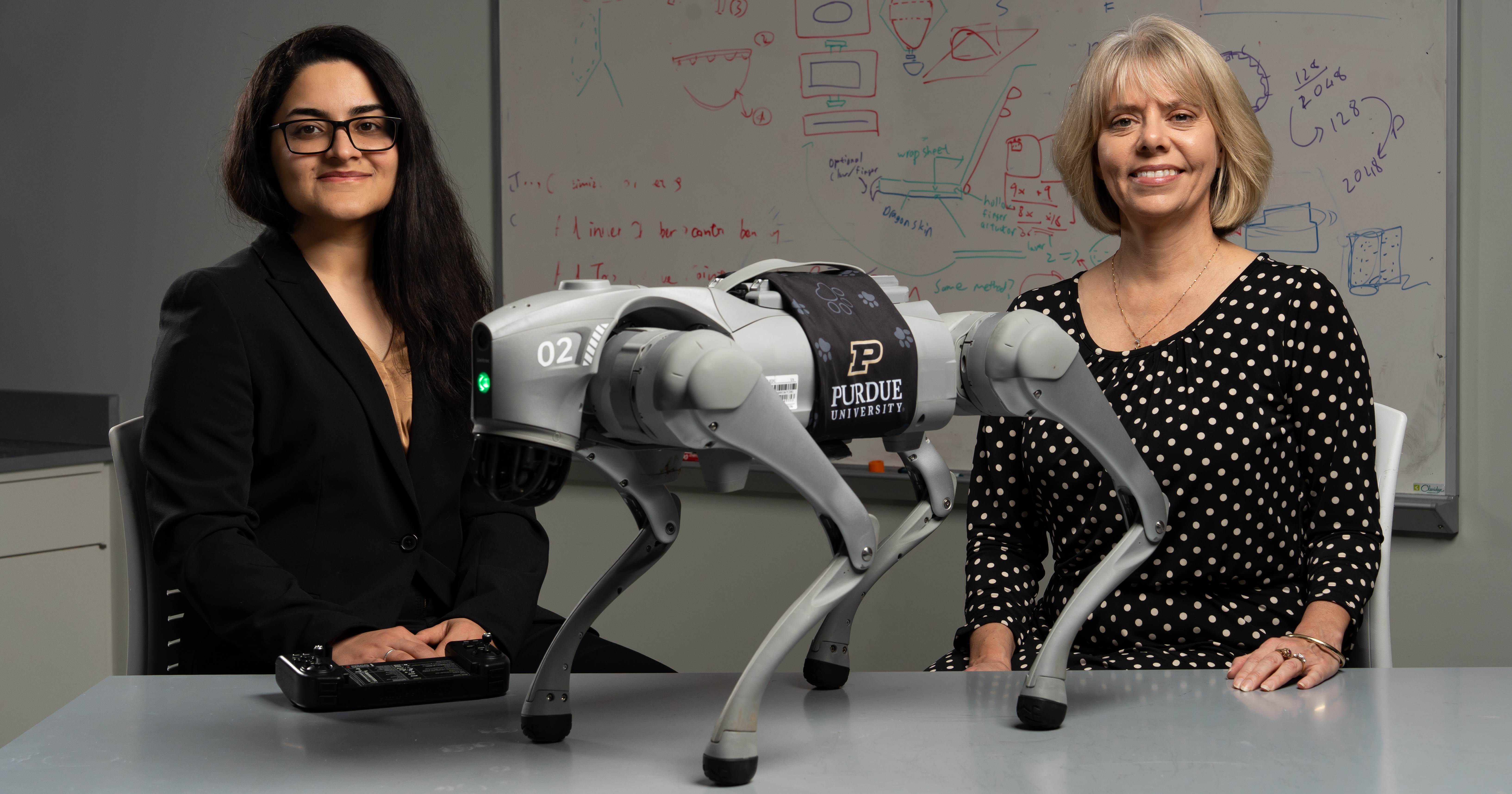 Kaur and Hill stand by robotic dog on a table