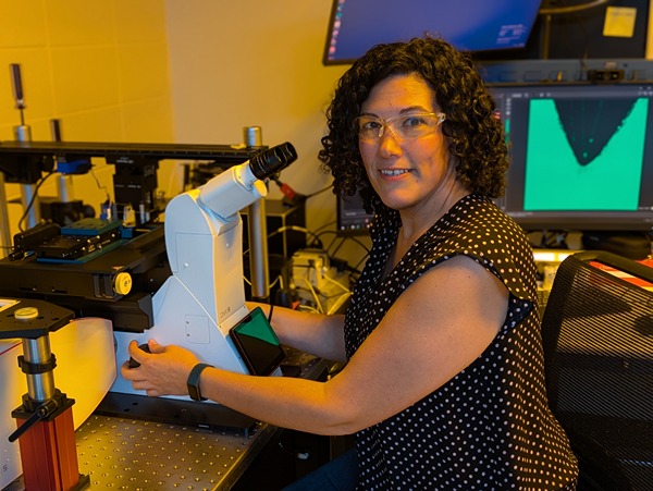 Chelsea Davis ears safety goggles and sits by a microscope