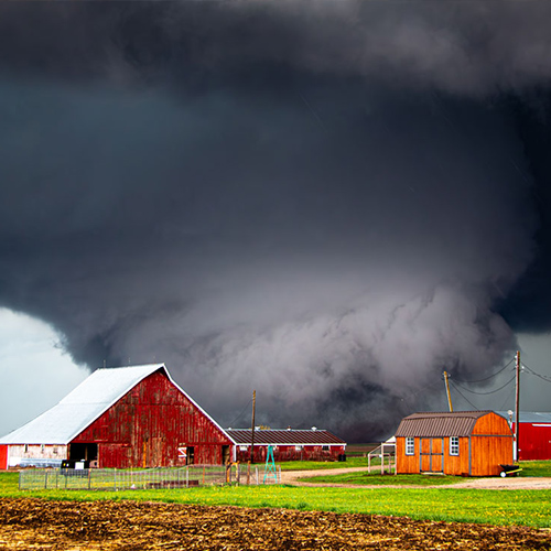 A dark tornado funnel is shown near a farm.
