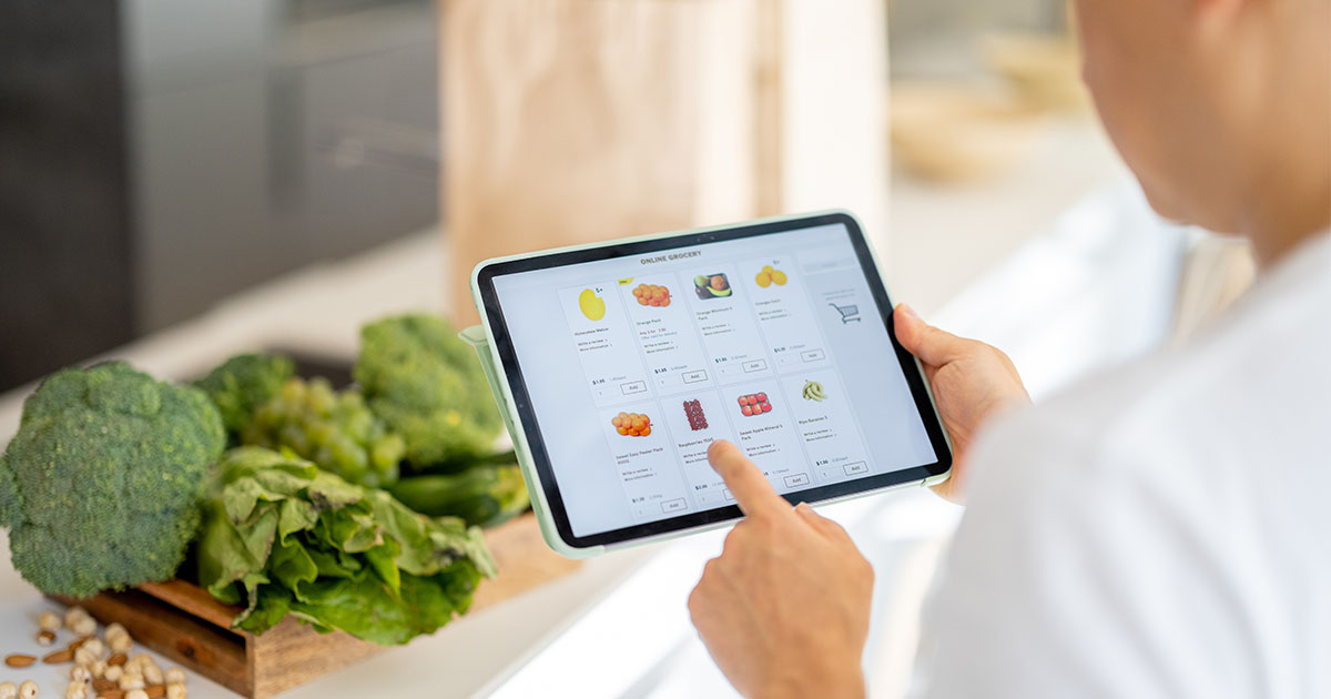Man in kitchen ordering groceries on a tablet and vegetables on counter