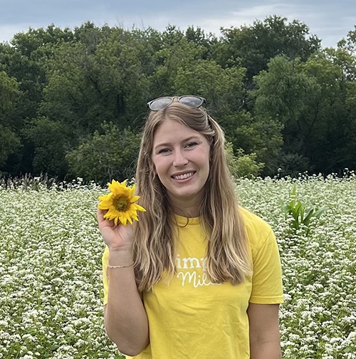 Monica Stampfli in a field holding a sunflower.