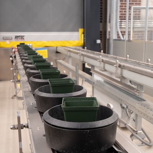 a conveyor belt loaded with empty green pots in front of a closed metal door in the greenhouses