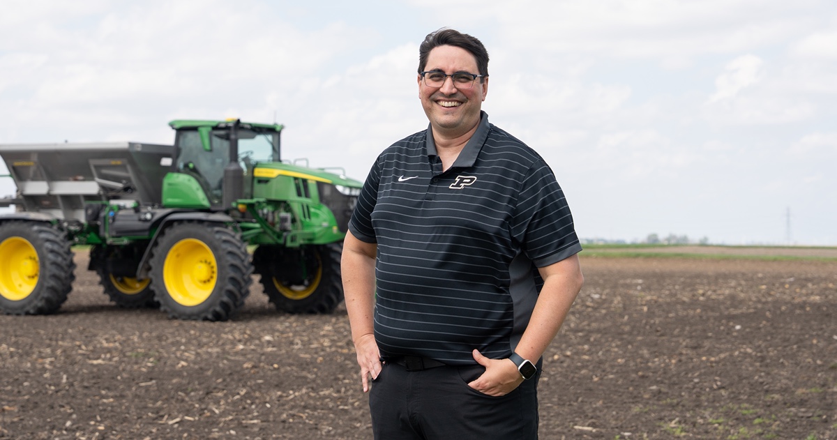 Man stands in field with farm machinery.
