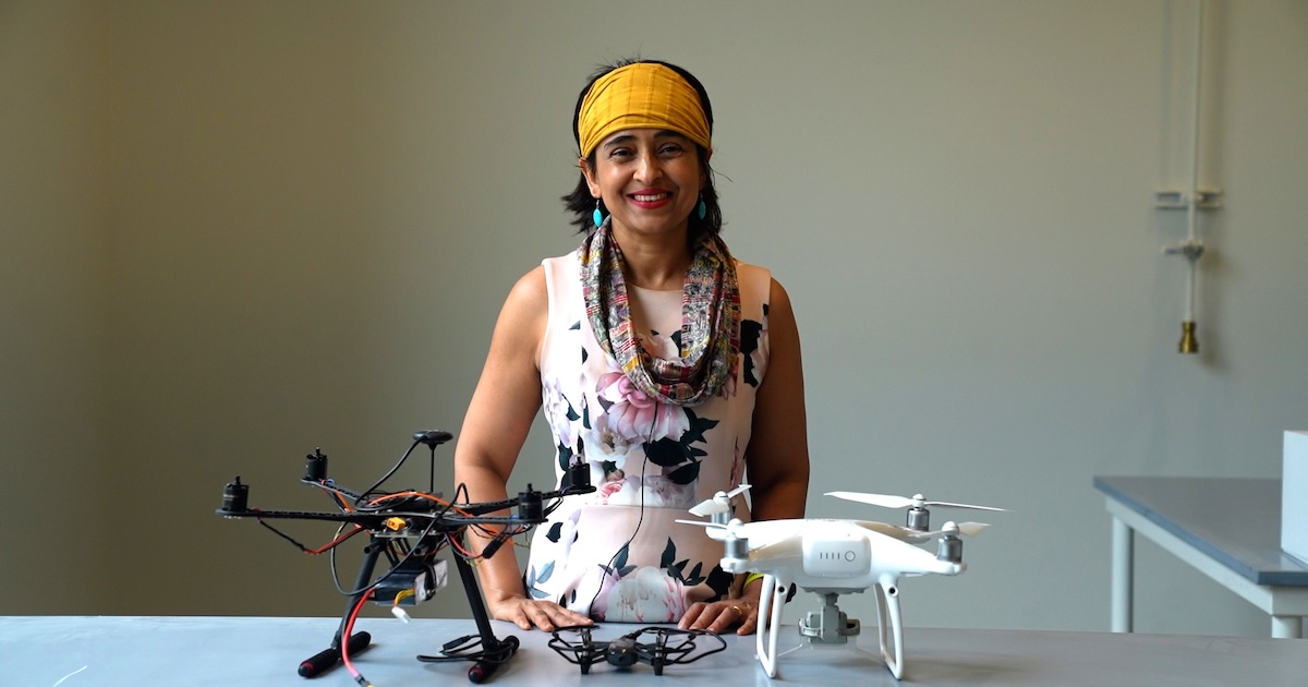 Somali Chaterji smiling behind a desk with two drones on it in her lab.