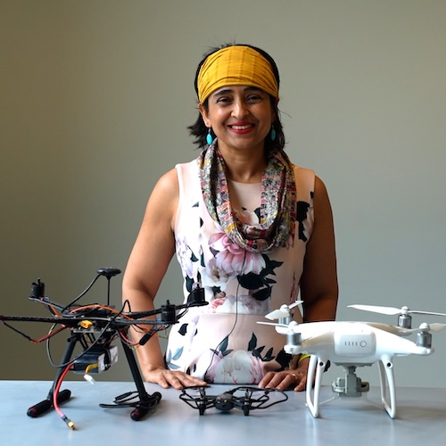 Somali Chaterji smiling behind a desk with two drones on it in her lab.