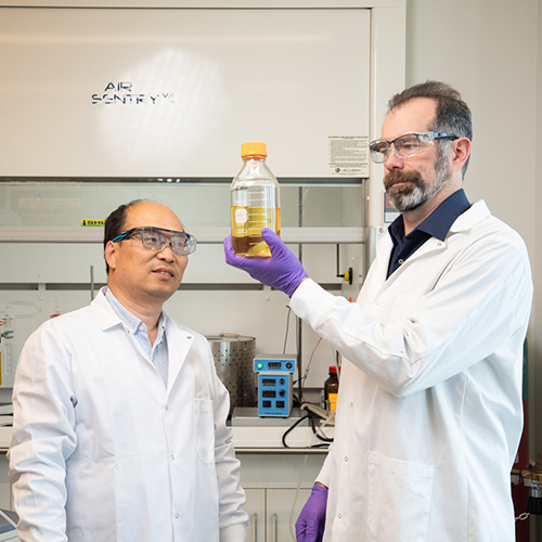Junli Liu and Nathan Mosier hold up a bottle of biokerosene in the lab