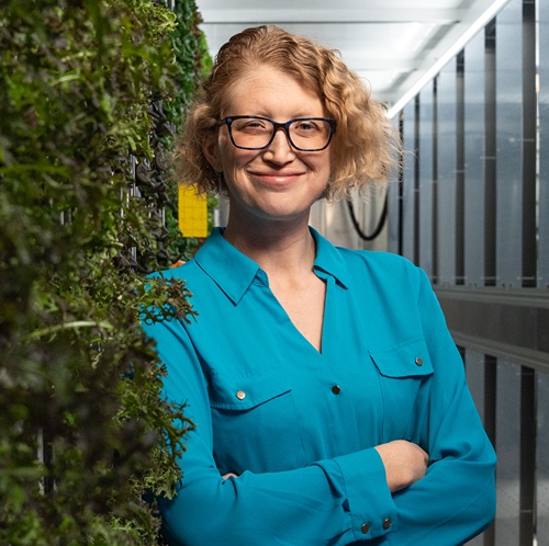 Caitlin Proctor stands next to the Overbeck Controlled Environment Agricultural Facility’s vertical hydroponic system