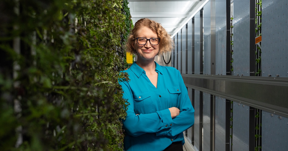 Caitlin Proctor stands next to the Overbeck Controlled Environment Agricultural Facility’s vertical hydroponic system
