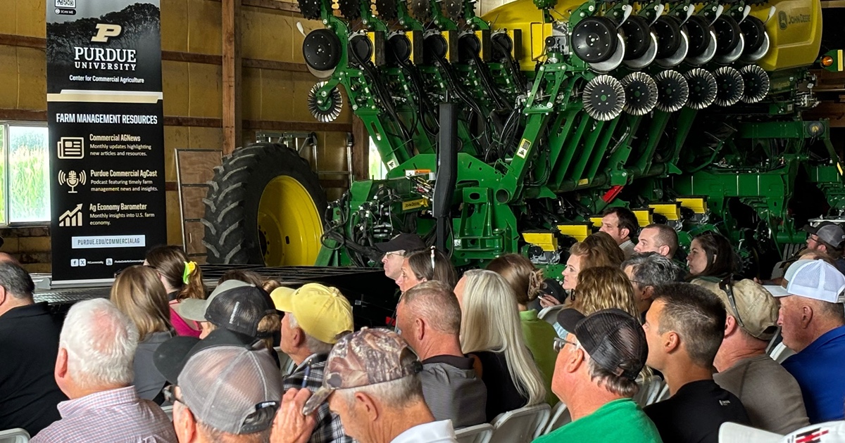 audience seated in a barn at the 2024 Purdue Farm Management Tour event next to a large green John Deere planter