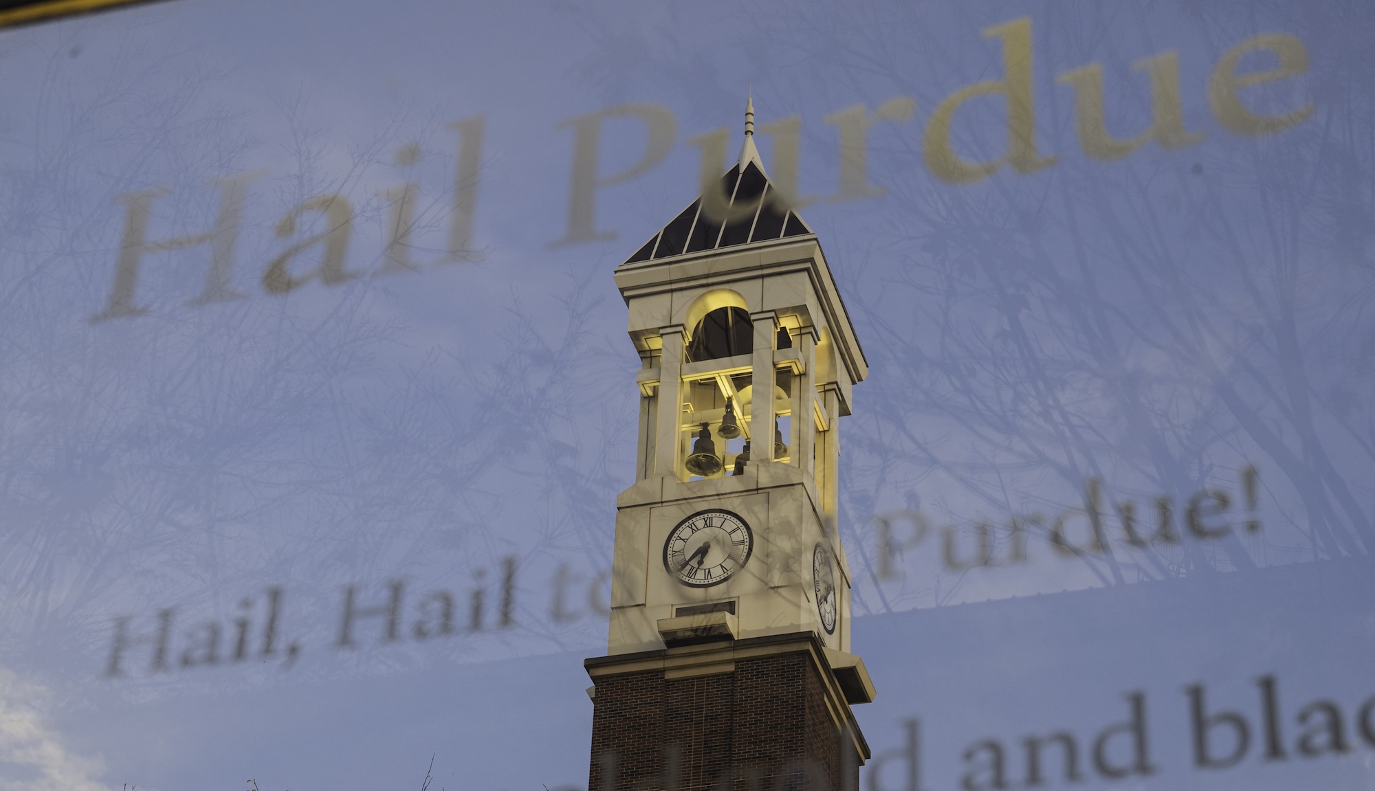 The bell tower reflecting in a mirrored sign that displays Purdue University’s fight song lyrics.