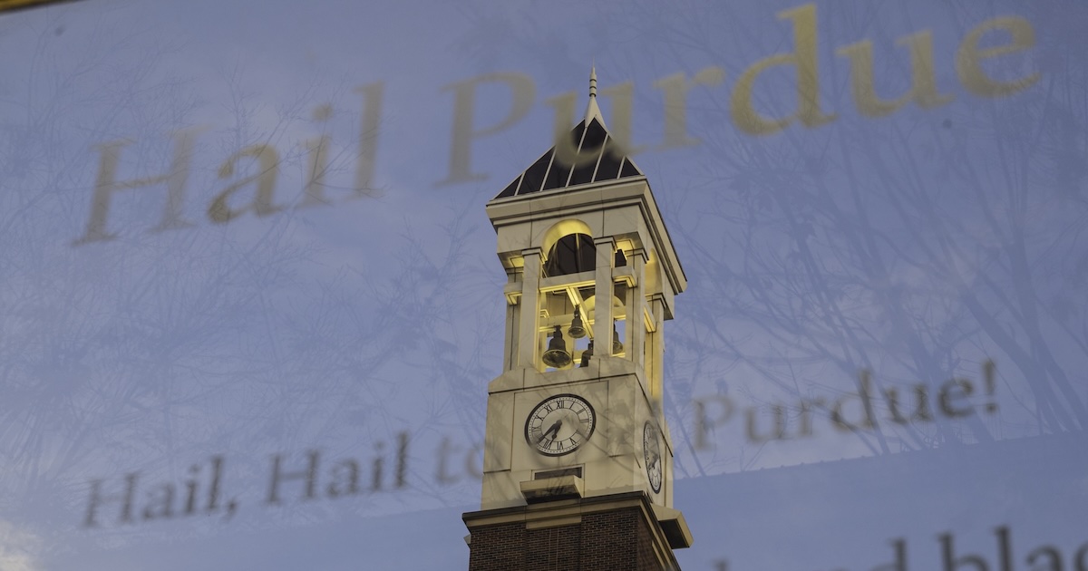 The bell tower reflecting in a mirrored sign that displays Purdue University’s fight song lyrics.