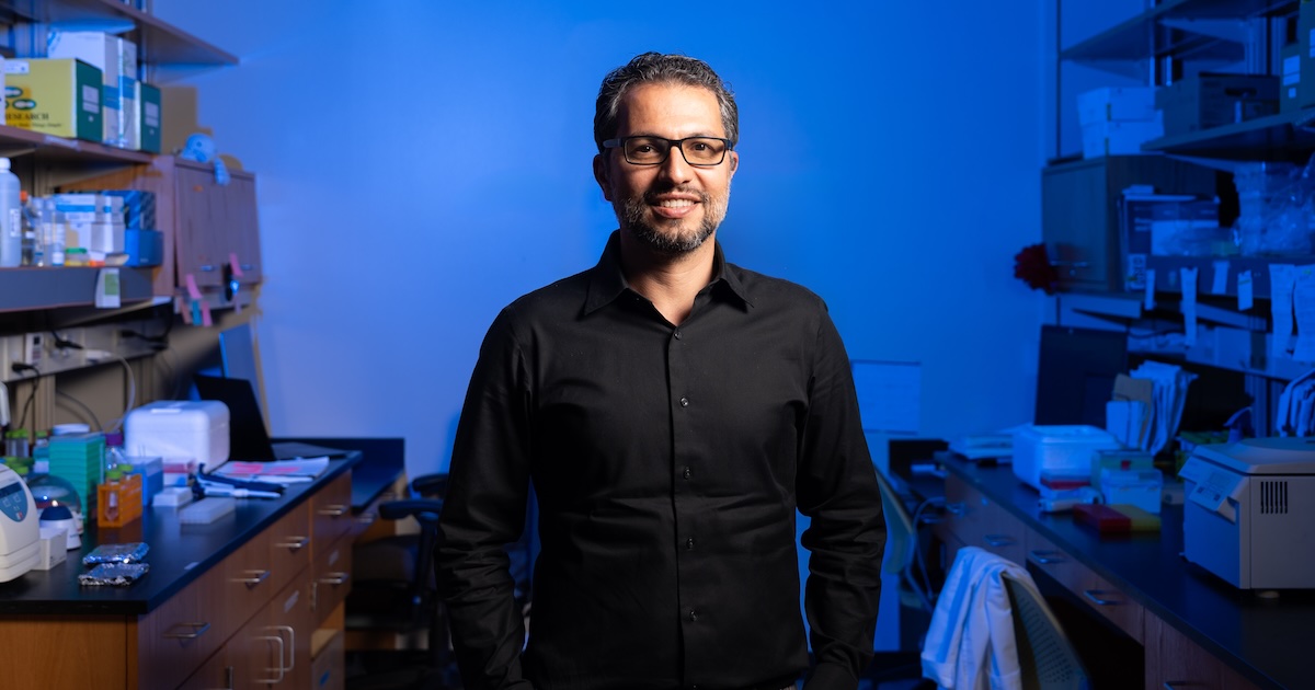 Majid Kazemian in his lab, standing in front of a desk, smiling.