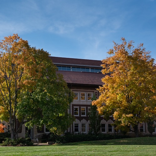 Red brick building on Purdue University's campus with two yellow and orange trees on either side.