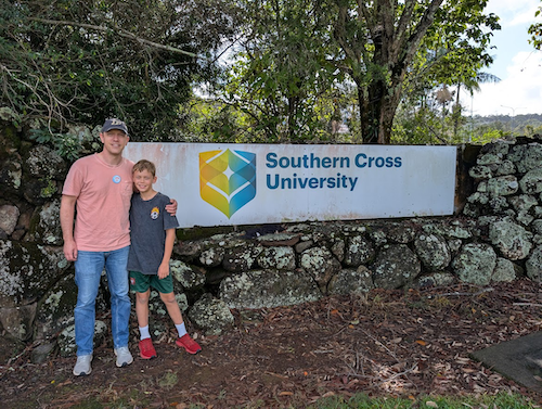 Stephen Meyers and his son posing at a sign that reads, "Southern Cross University."