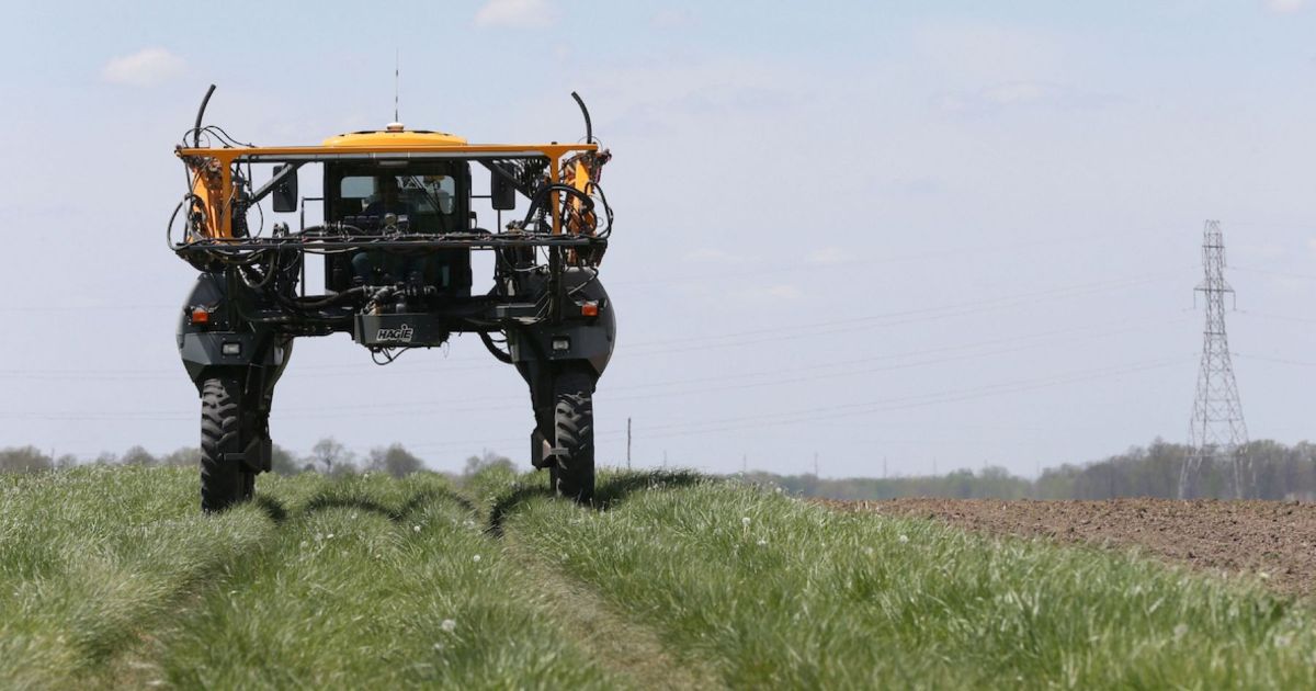 High-clearance agricultural sprayer in a field with electrical transmission tower and lines in background
