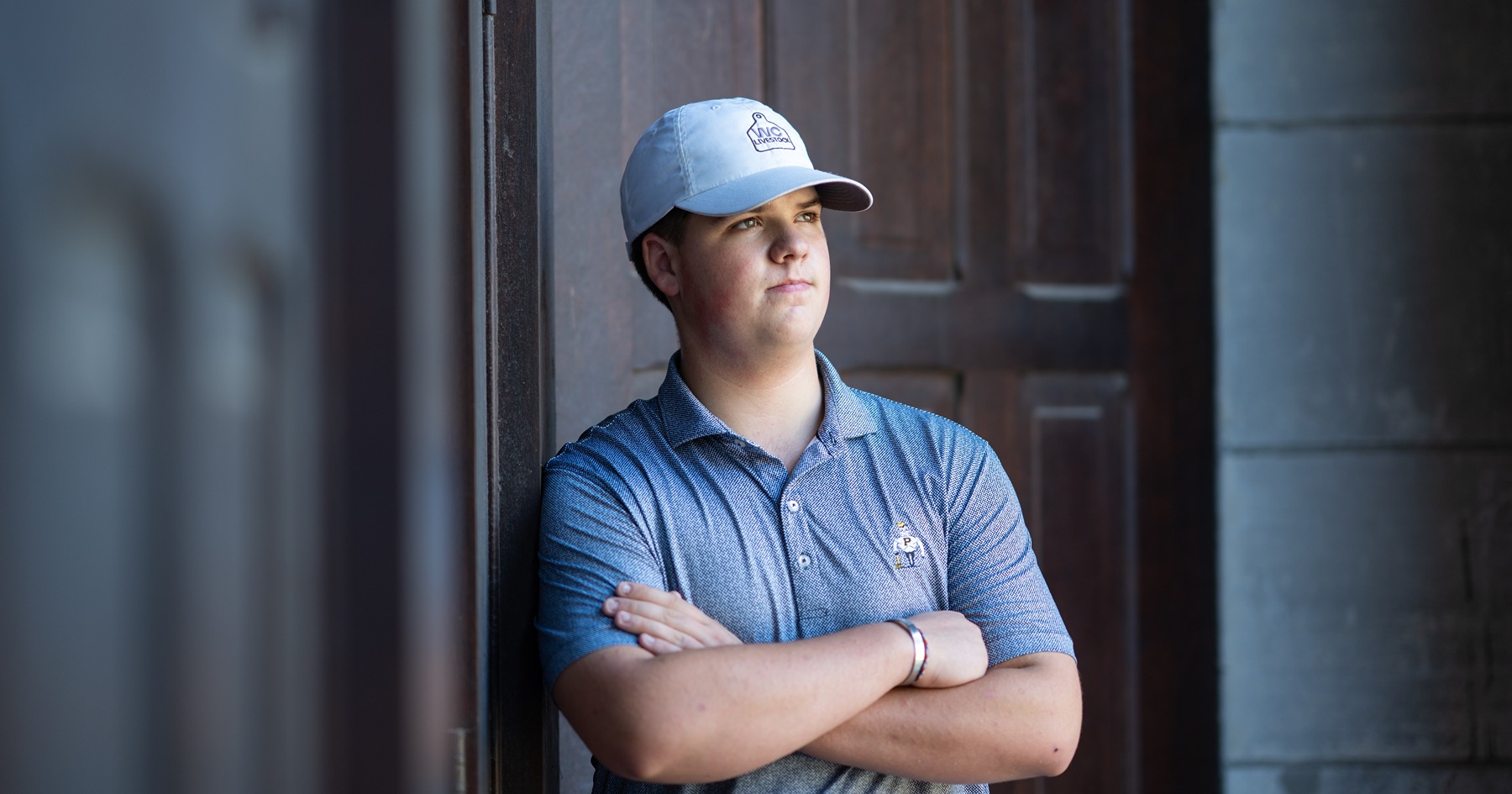 Brody Cox poses with arms crossed in front of Pfendler Hall