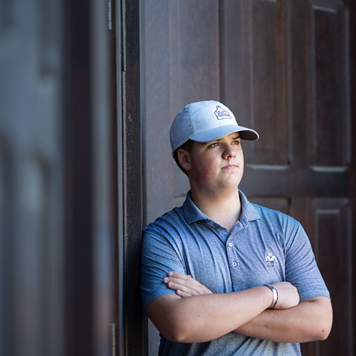 Brody Cox poses with arms crossed in front of Pfendler Hall