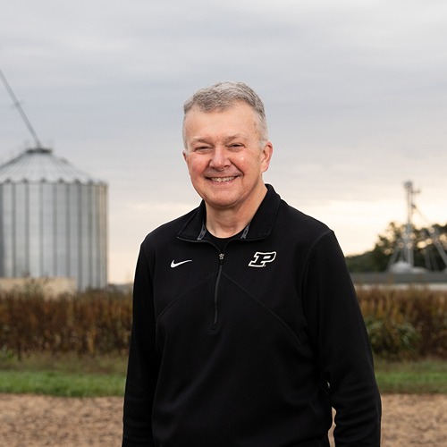 Man stands in front of harvested field and grain bins