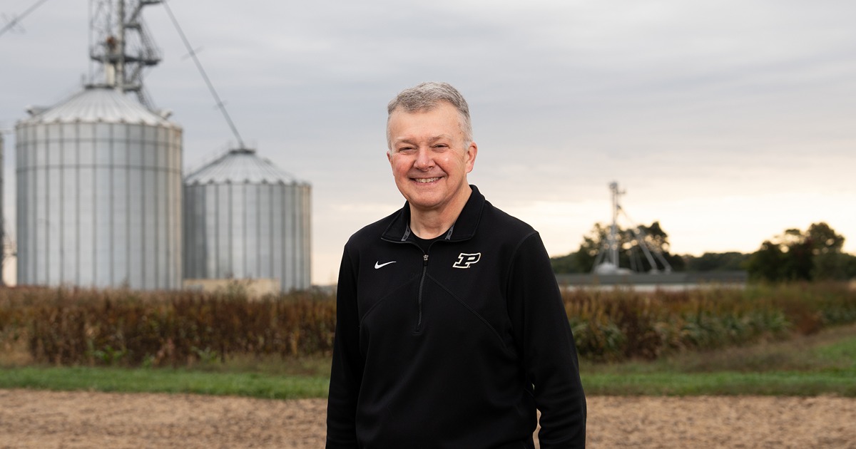 Man stands in front of harvested field and grain bins