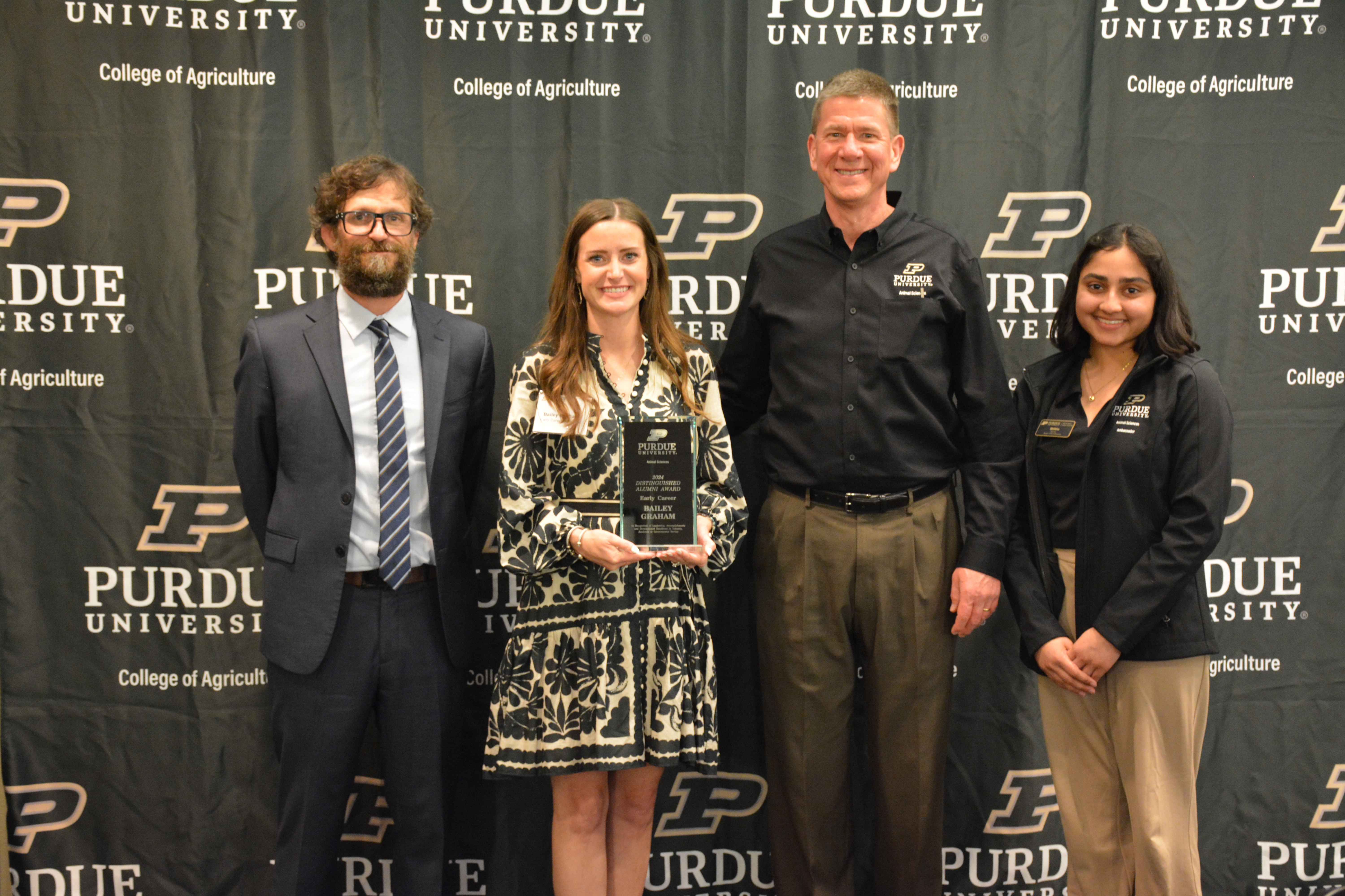 Bailey Graham holding award. Barry Delks, Dr. Paul Ebner, and Shikha Adhikari stand with her.