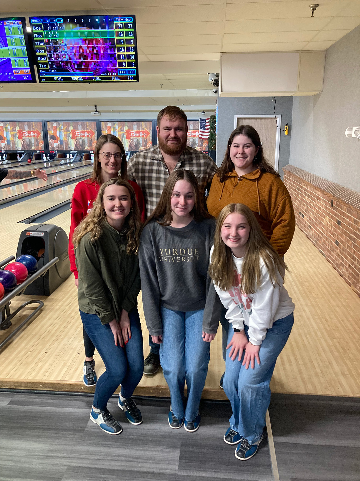 Members of Heather Neave’s lab pose together at a bowling alley, standing in front of bowling lanes and scoreboards.