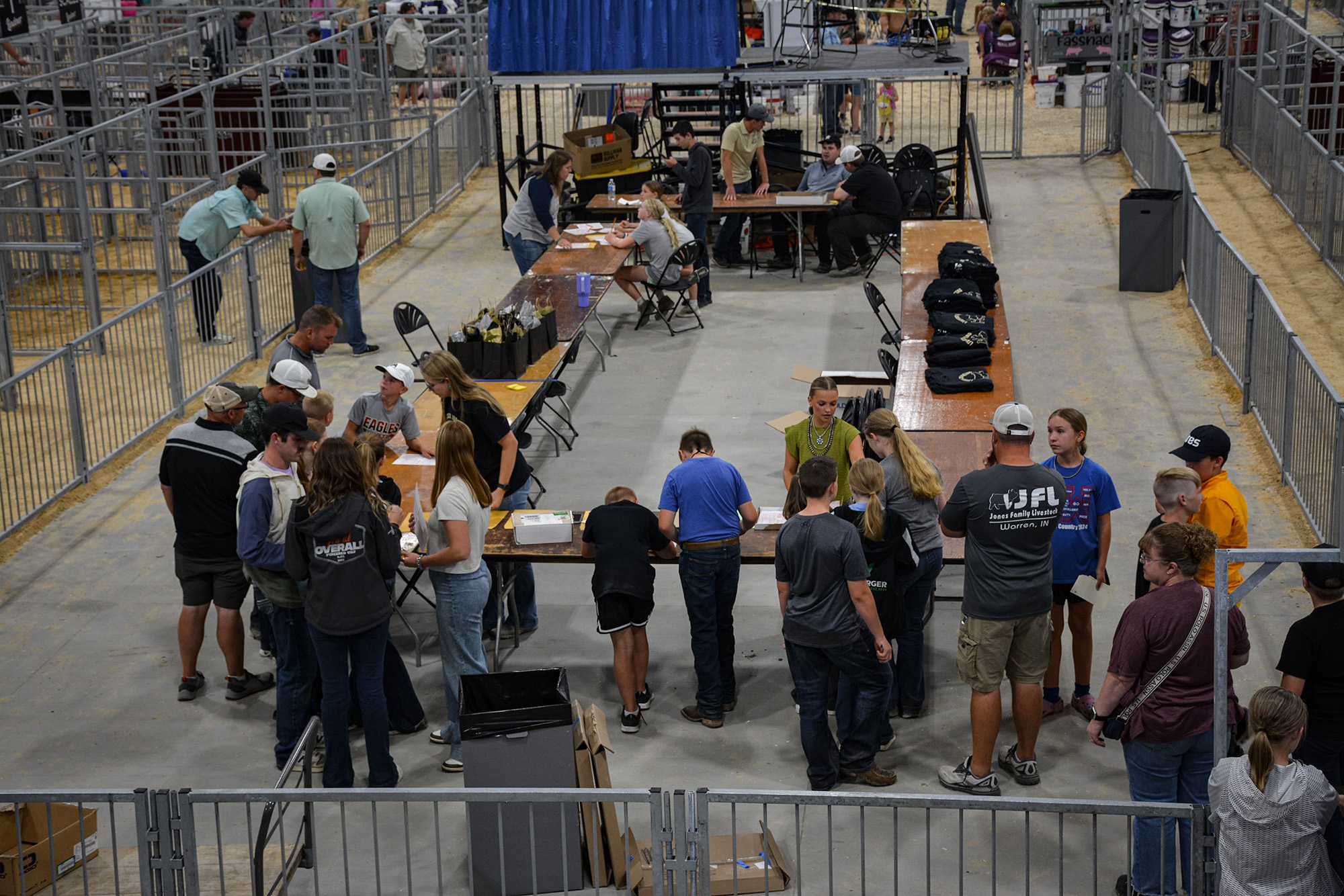 Participants filling out forms at registration tables during an indoor livestock judging event, surrounded by metal railings and event materials.