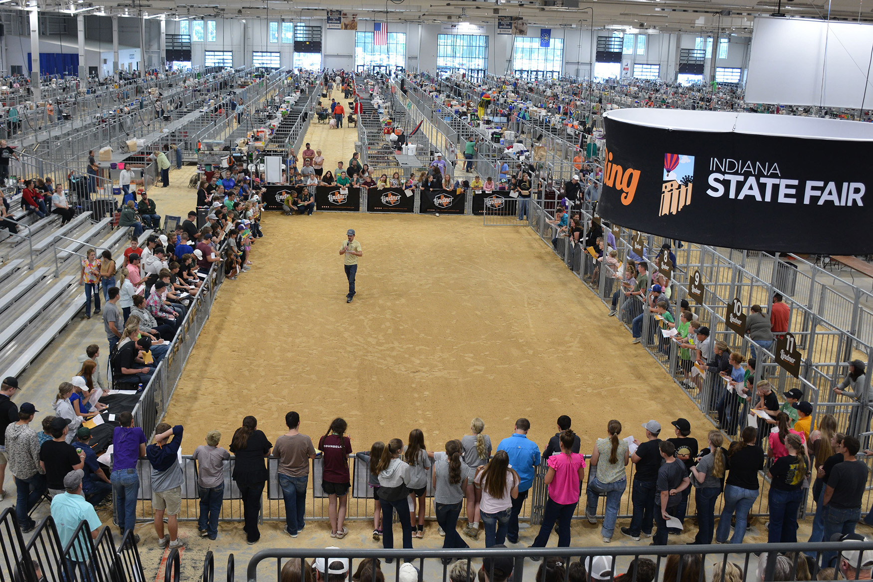 Crowd gathered in a large indoor arena at the Indiana State Fair, with bleachers full of spectators and a central sandy area used for livestock exhibitions.