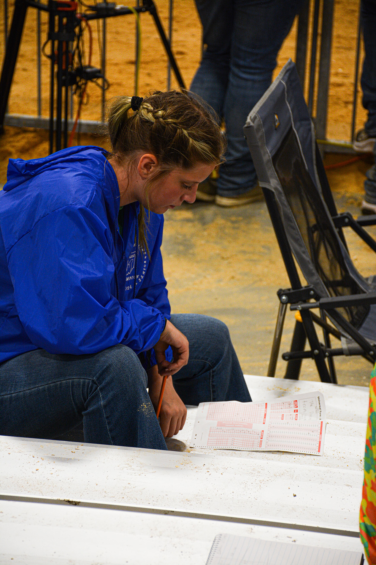 Person in a blue jacket sitting on bleachers, holding a pencil and reviewing a paper.